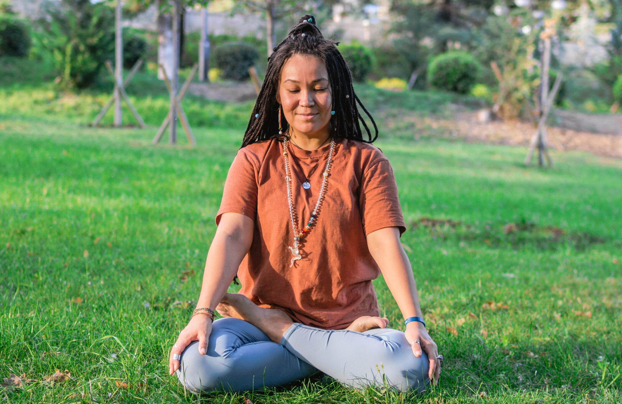 Young woman is sitting in the lotus position and meditating in a park. Concept of healthy lifestyle.